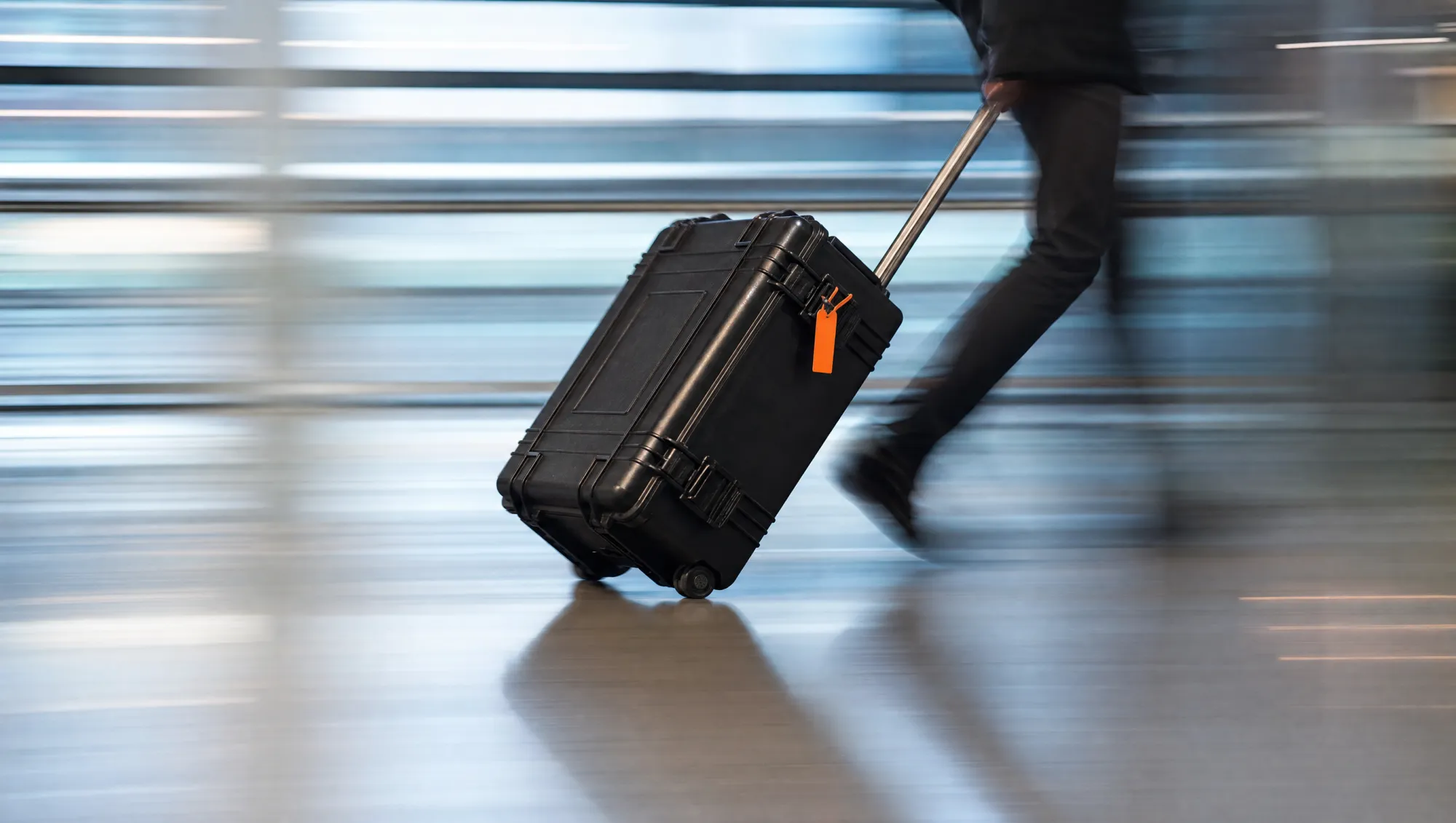 A hard-shell transit case being pulled at speed through an airport terminal